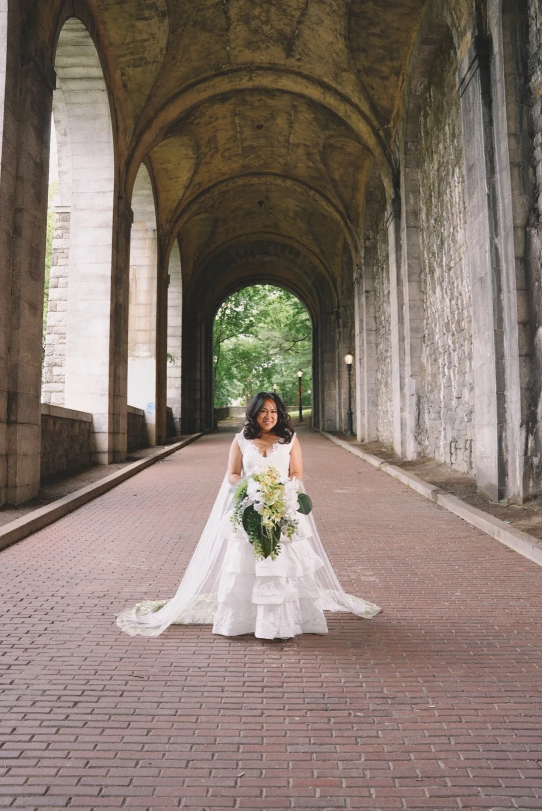 A bride holding her bouquet beneath the arches at Bethesda Terrace