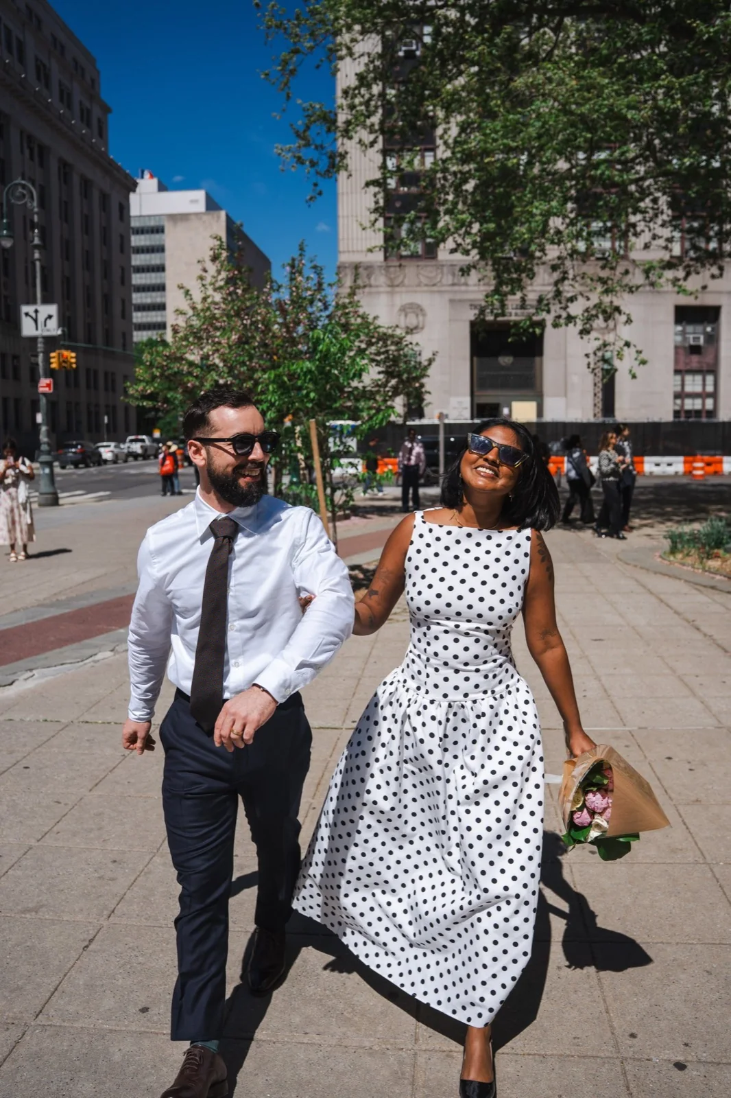 A couple walking and smiling on a New York City sidewalk after their City Hall wedding